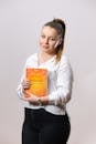 Confident young woman holding a marketing book, smiling in a studio setting, signaling readiness for learning and business.