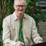 Elderly man enjoying remote work on a laptop in a garden setting.